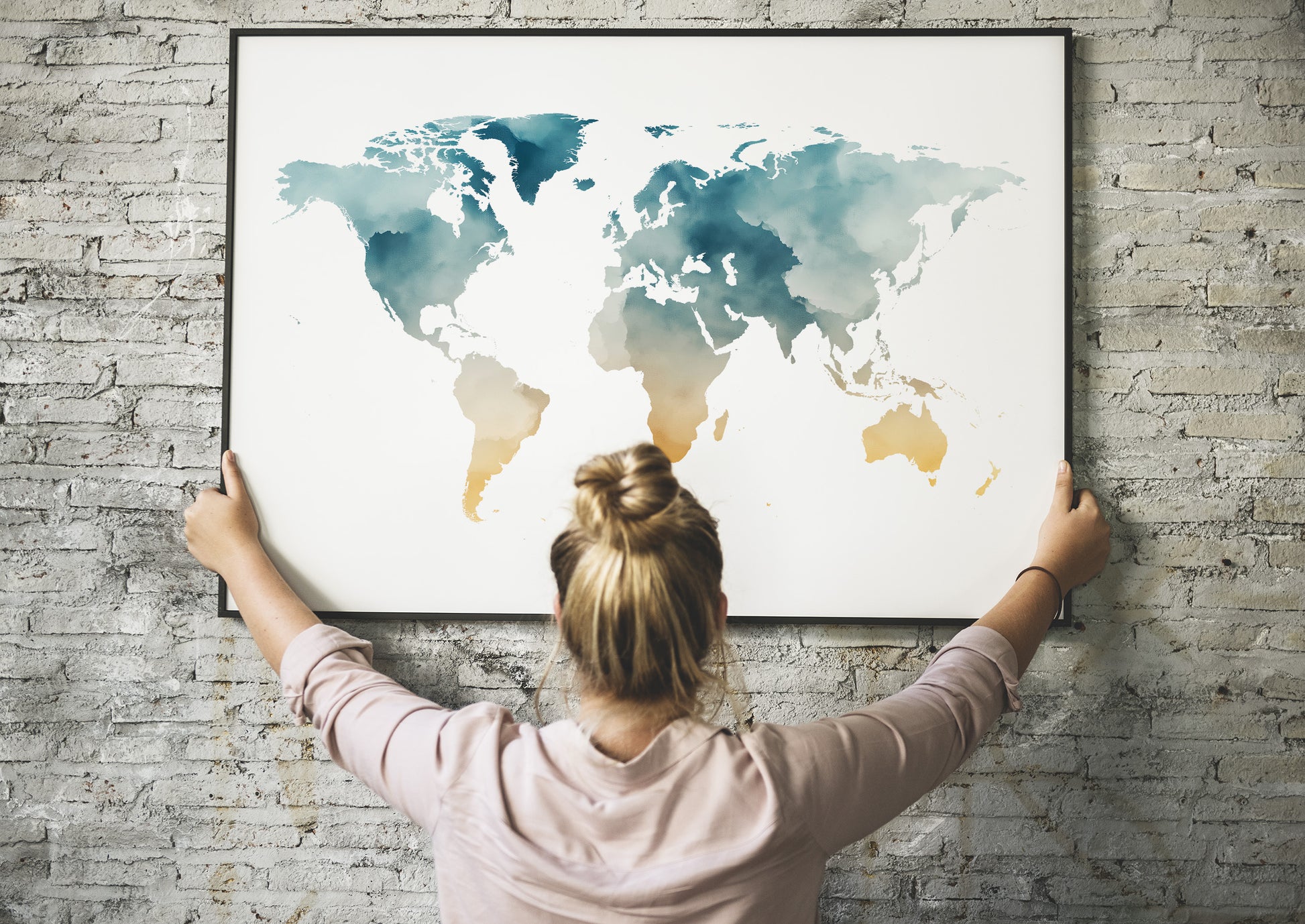 Person holding a framed world map against a brick wall