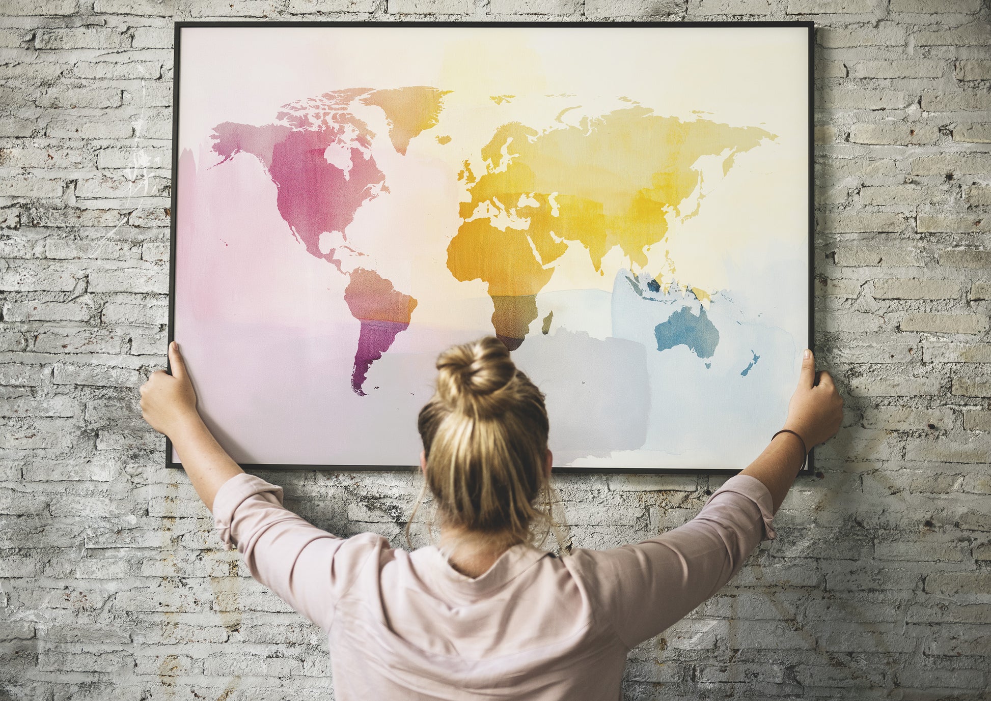 Person hanging a colorful world map on a brick wall