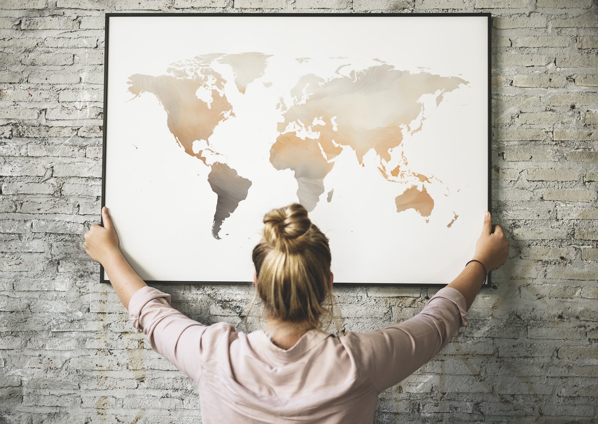 Person holding a framed world map against a brick wall