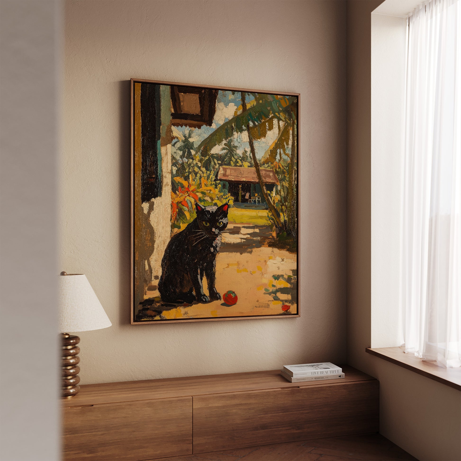 A framed painting of a black cat in a tropical garden setting, displayed on a beige wall above a wooden console table in a modern room.