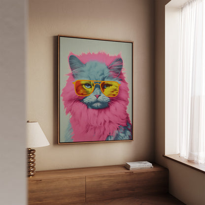 A framed wall art print showing a stylized blue-gray cat with bright pink fur and yellow sunglasses, displayed in a real interior setting above a wooden console table near a window.