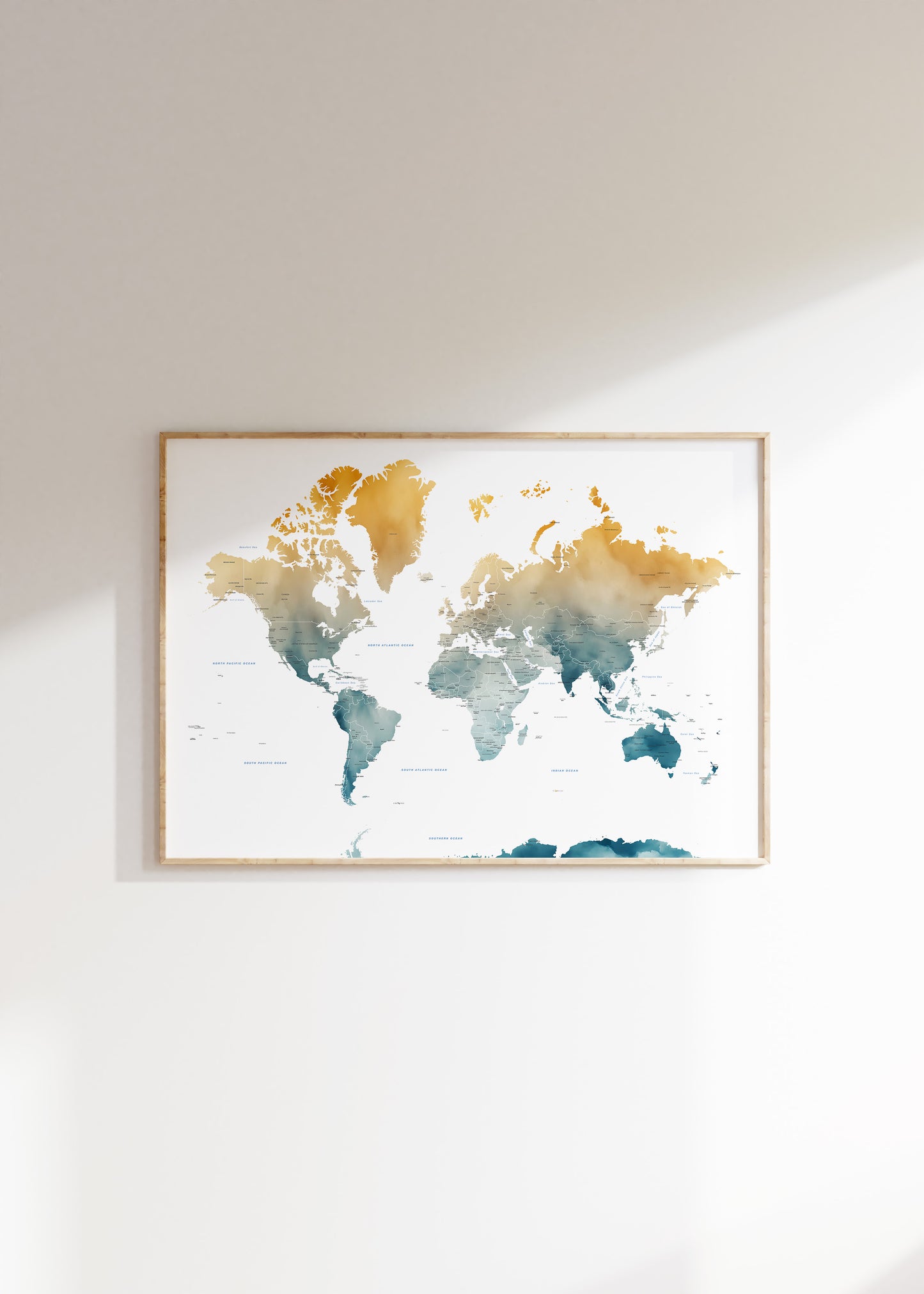 A framed world map watercolor print with gold, teal, and blue landmasses on a white background, hung on a light beige wall.