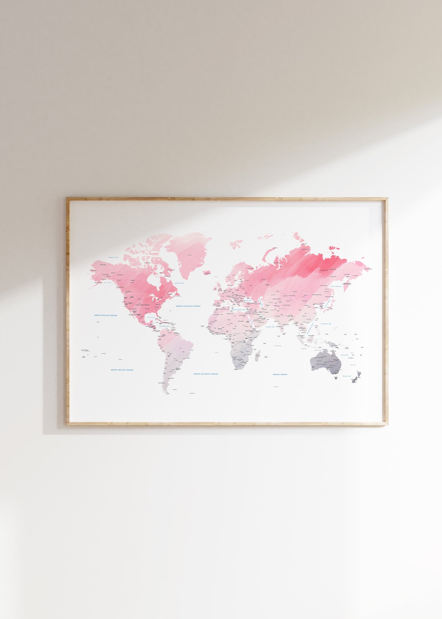 Framed world map with pink and gray watercolor design on a white wall.