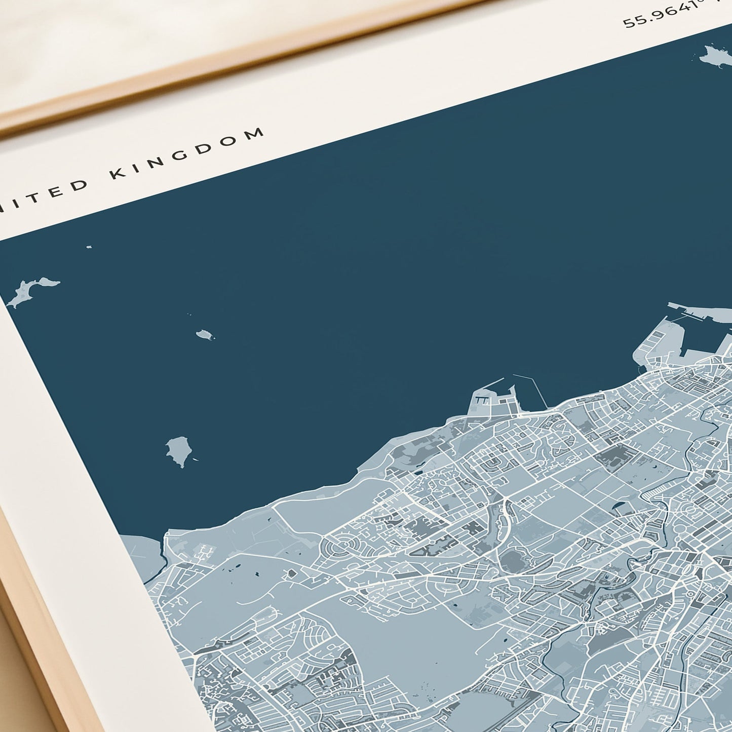A framed Edinburgh city map print with a cream border and dark blue sea area, styled on a tabletop next to a beige gift box.