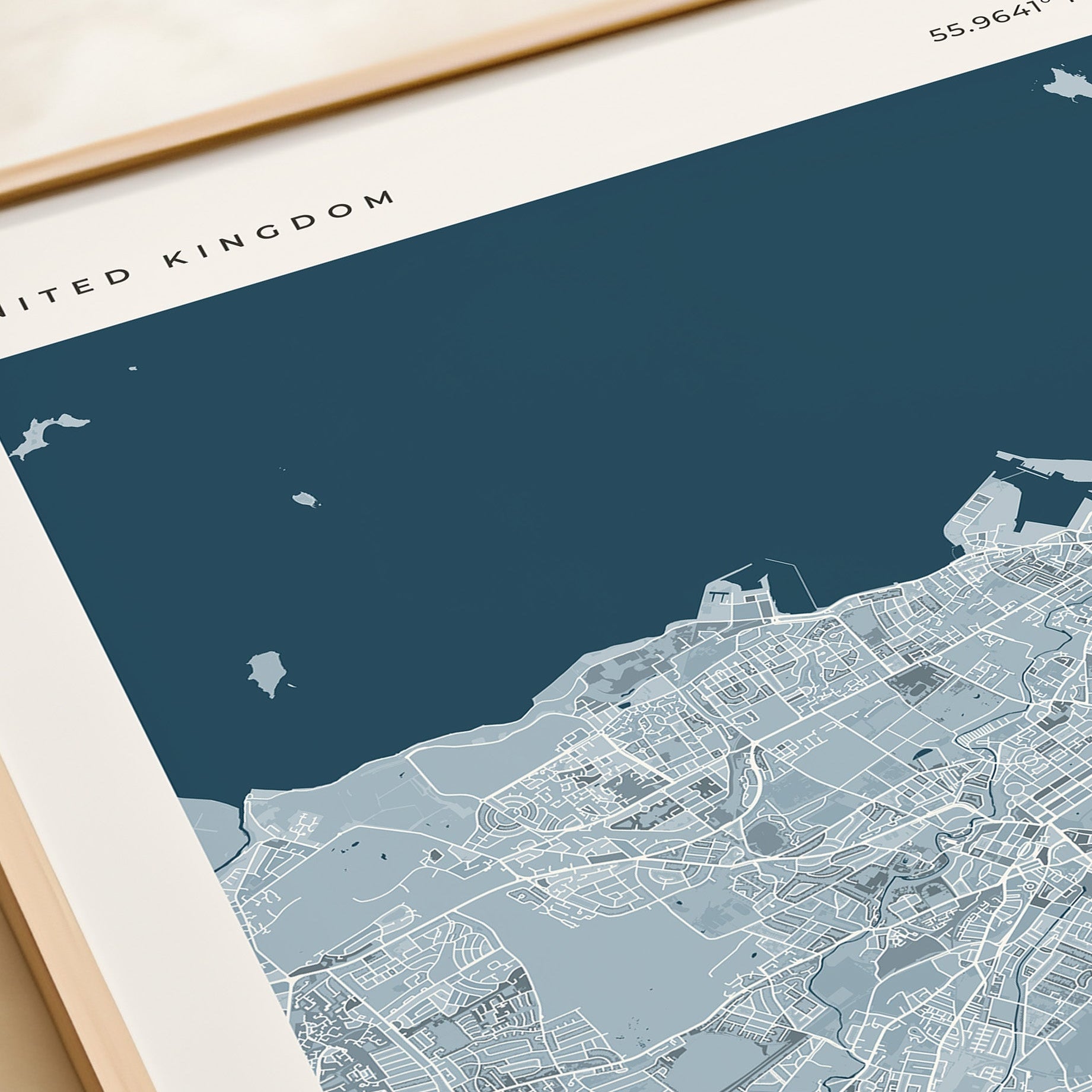 A framed Edinburgh city map print with a cream border and dark blue sea area, styled on a tabletop next to a beige gift box.