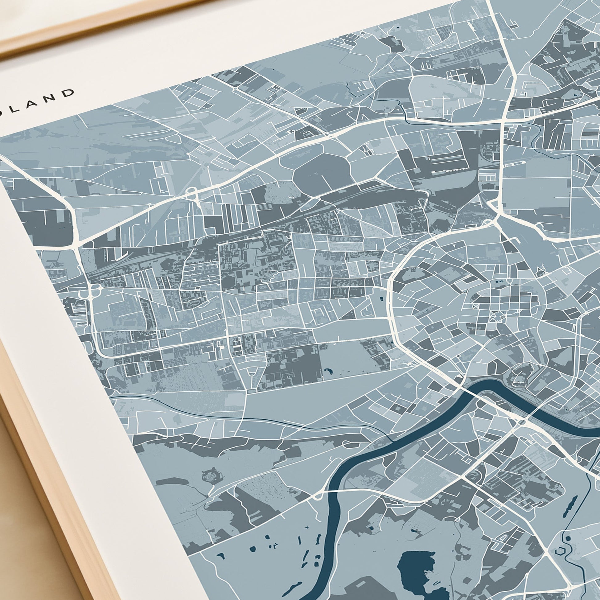 A framed minimalist map print of Krakow, Poland, featuring a light blue and gray cartographic design with a dark blue river and the city name 'KRAKOW' at the bottom, styled on a beige tabletop next to a cream-colored gift box.