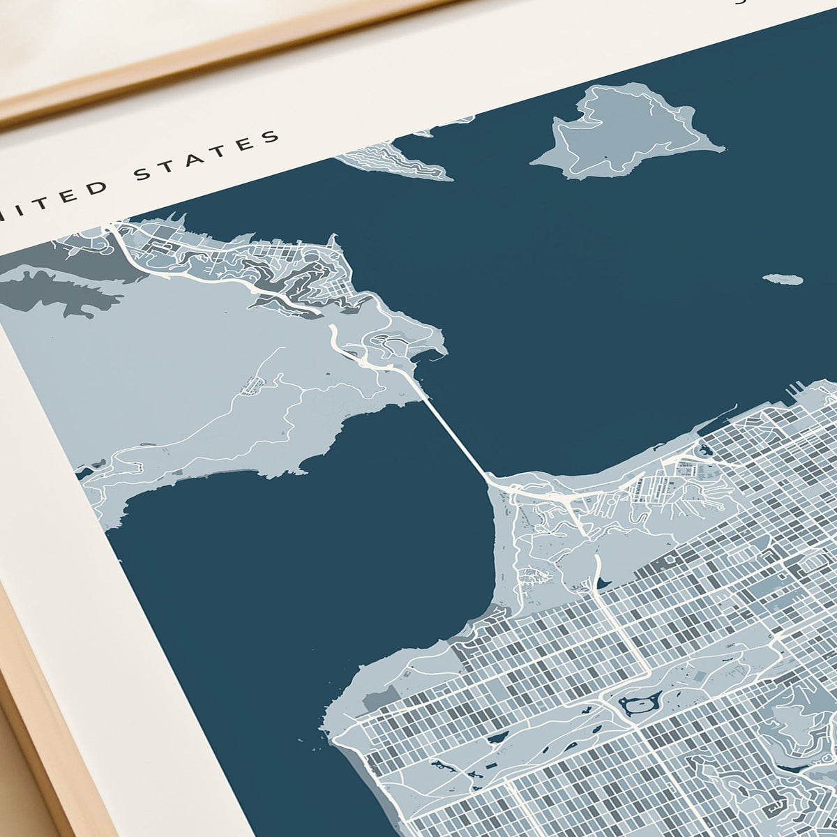 A framed San Francisco city map print with a navy blue background and light gray street details, displayed on a beige tabletop next to a rolled cream document.
