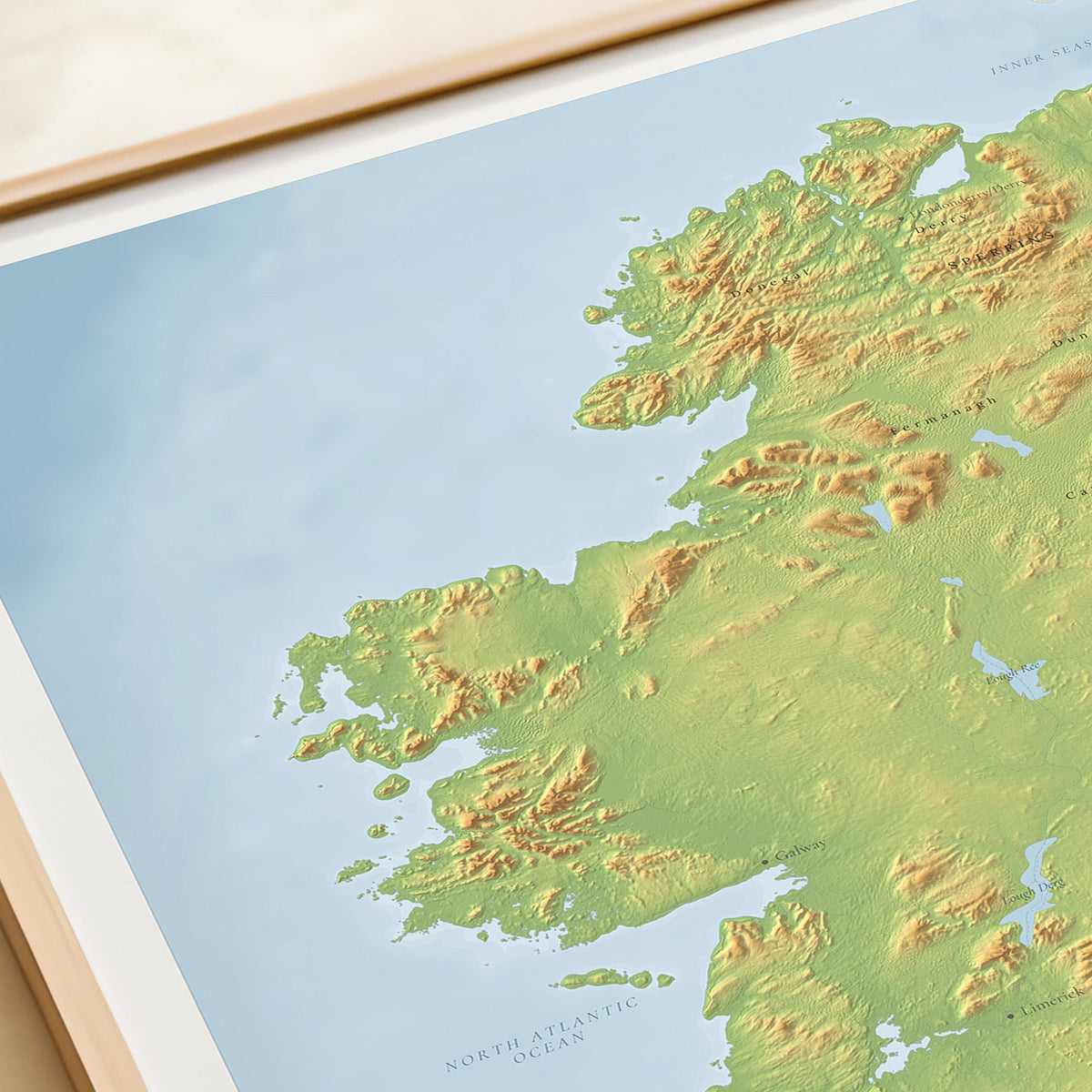 A close-up of a framed relief map of Ireland and the surrounding North Atlantic Ocean, showing green and tan topographic shading against a light blue sea background.