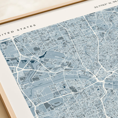 A framed modern city map print of the United States, featuring a detailed street grid and waterways in shades of slate blue, gray, and white, with a light wood frame.