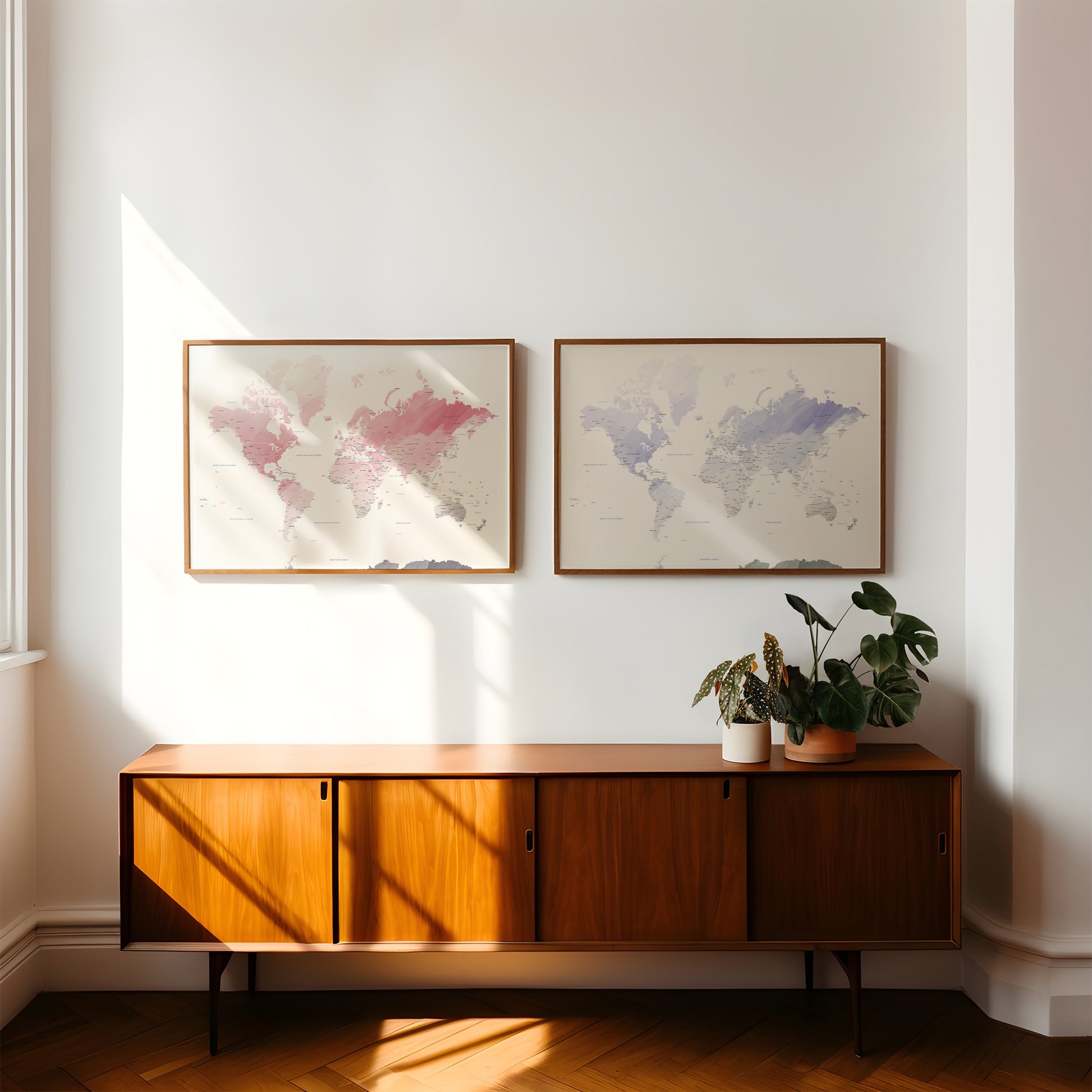 Two framed world maps hang on a white wall above a mid-century modern wooden sideboard with potted plants, in a sunlit room with herringbone wood floors.