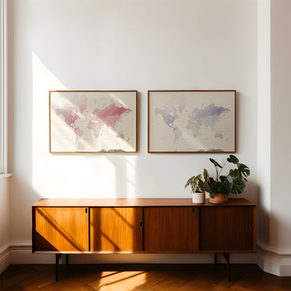 Two framed world maps hang on a white wall above a mid-century modern wooden sideboard with potted plants, in a sunlit room with herringbone wood floors.