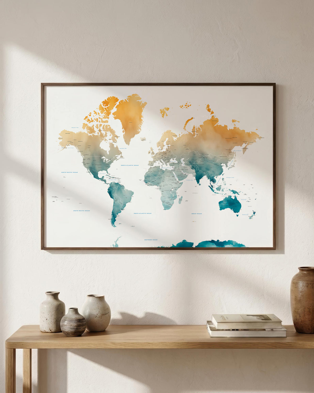 Framed world map wall art with a watercolor finish in teal and mustard tones, hanging on a light beige wall above a wooden console table with decorative vases and books.