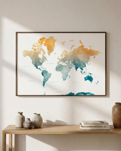 Framed world map wall art with a watercolor finish in teal and mustard tones, hanging on a light beige wall above a wooden console table with decorative vases and books.