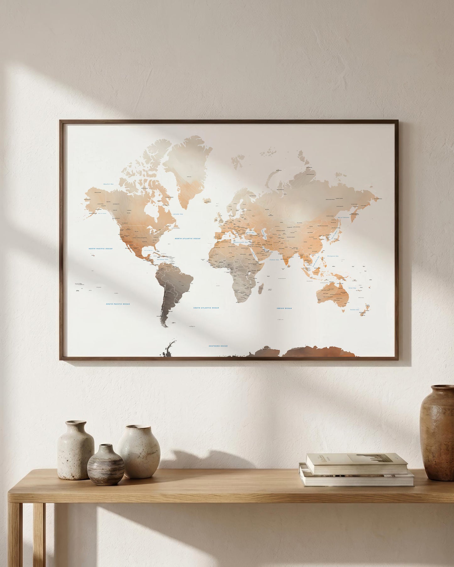 A framed world map print with a minimalist design hangs on a textured beige wall above a light wood console table styled with ceramic vases and books.