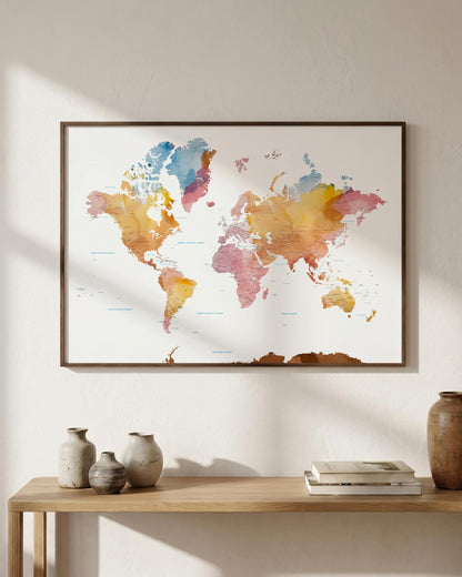 A framed world map watercolor print hangs on a light beige wall above a wooden console table with decorative vases and books. The map features soft watercolor continents in blue, yellow, pink, orange, and brown tones.