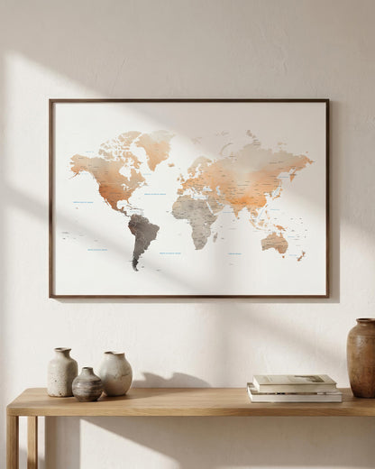 A framed world map print with a minimalist design hangs on a light beige wall above a wooden console table styled with vases and books. The map features watercolor-style continents in warm beige, brown, and gray tones.