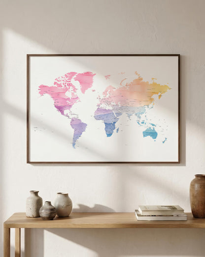 A framed world map art print with a pastel multicolor gradient hangs on a textured off-white wall above a wooden console table styled with vases and books.