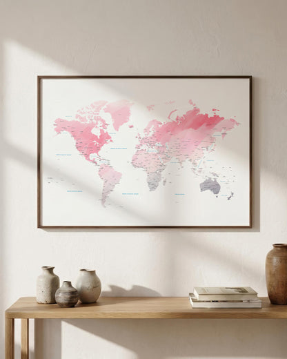 A framed world map print with pink and gray watercolor-style continents hangs on a light beige wall above a wooden console table with vases and books.