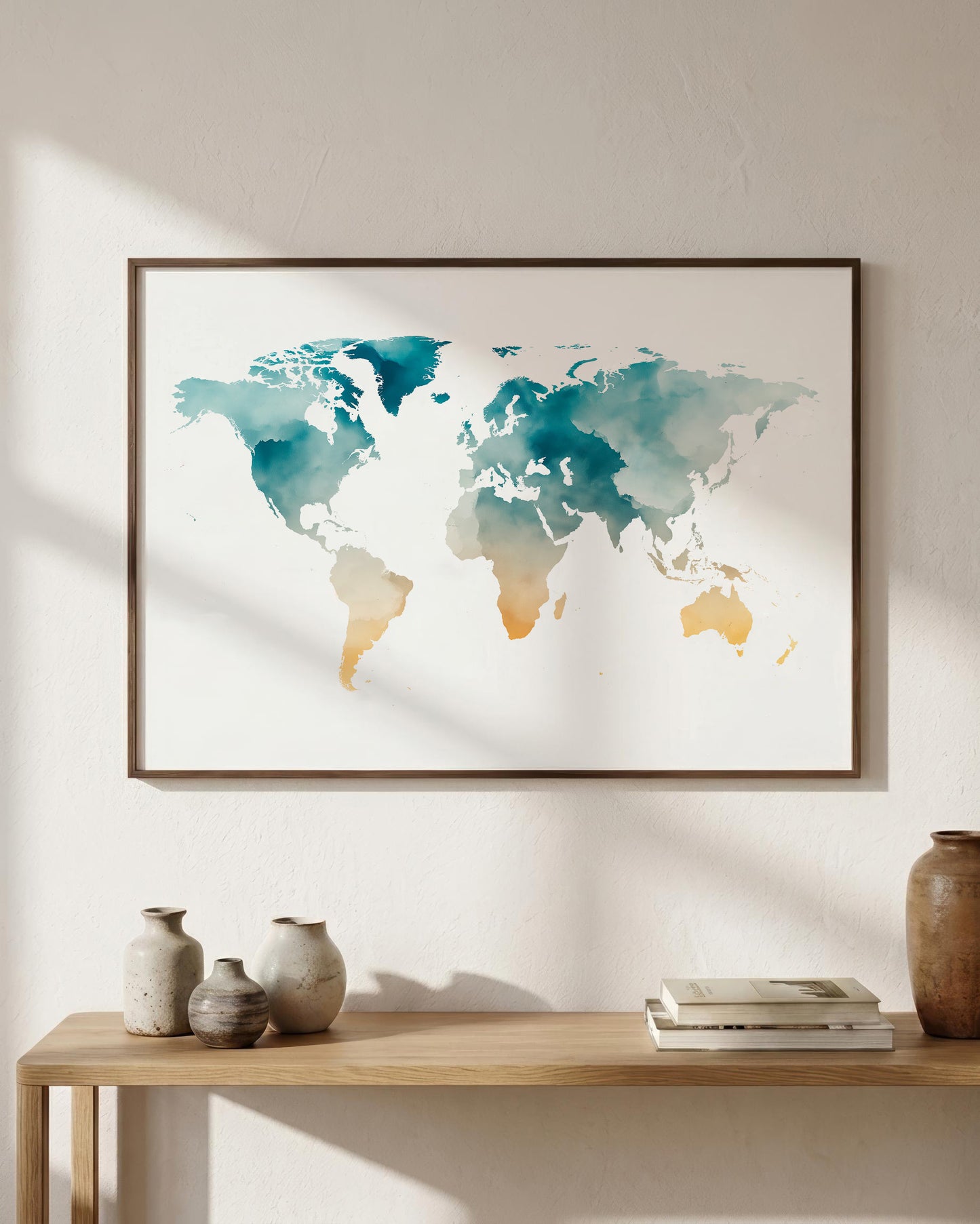 A framed world map watercolor print in teal and gold tones, displayed on a light beige wall above a wooden console table with decorative vases and books.