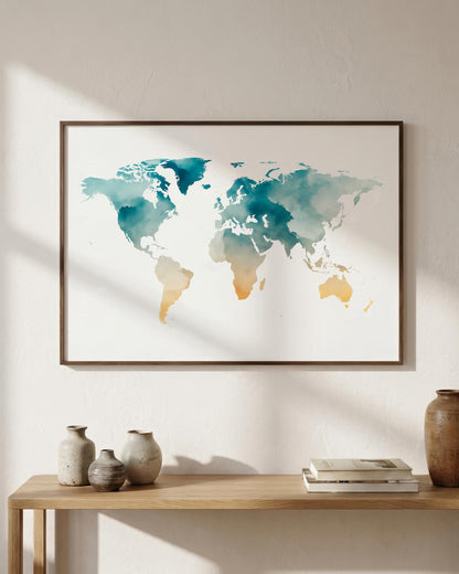 A framed world map watercolor print in teal and gold tones, displayed on a light beige wall above a wooden console table with decorative vases and books.
