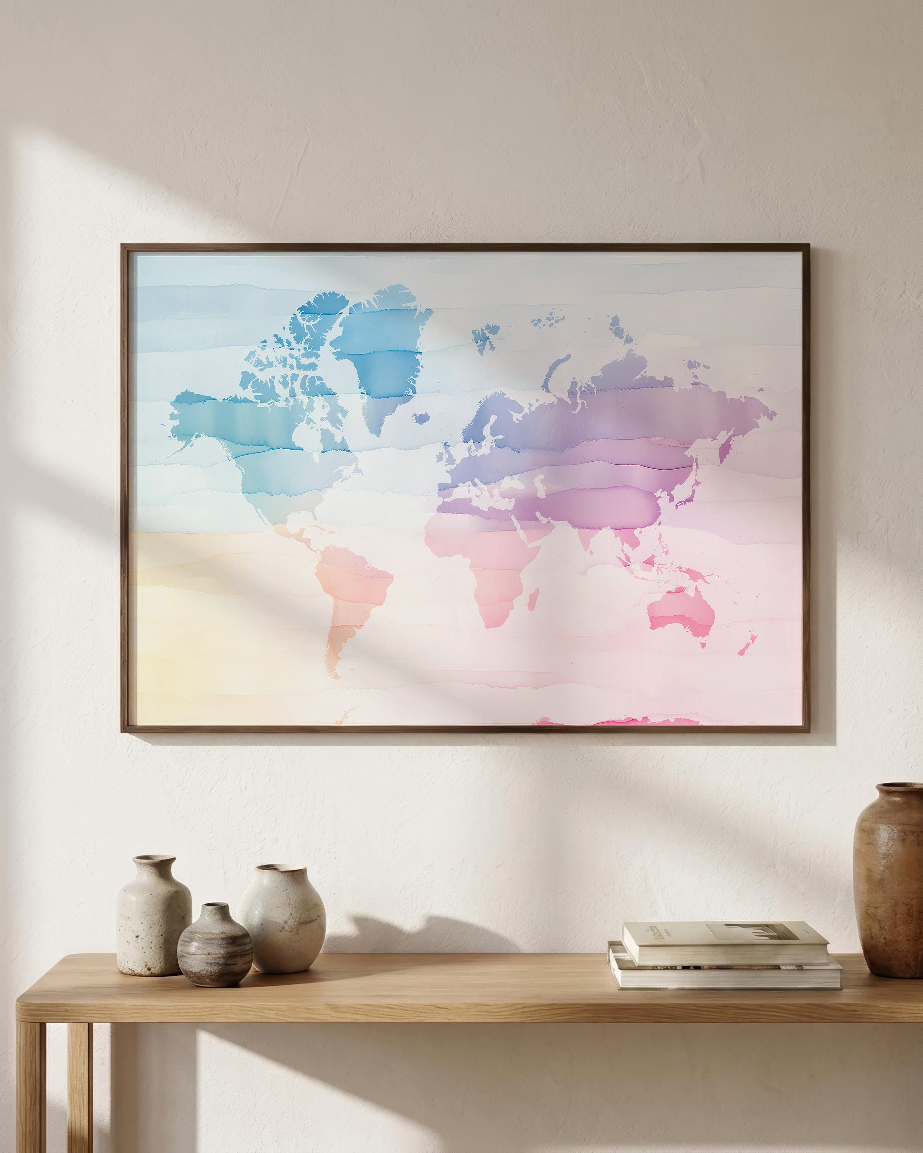 A framed world map art print with a pastel watercolor design in shades of blue, pink, purple, and yellow, hanging on a textured beige wall above a wooden console table with decorative vases and books.
