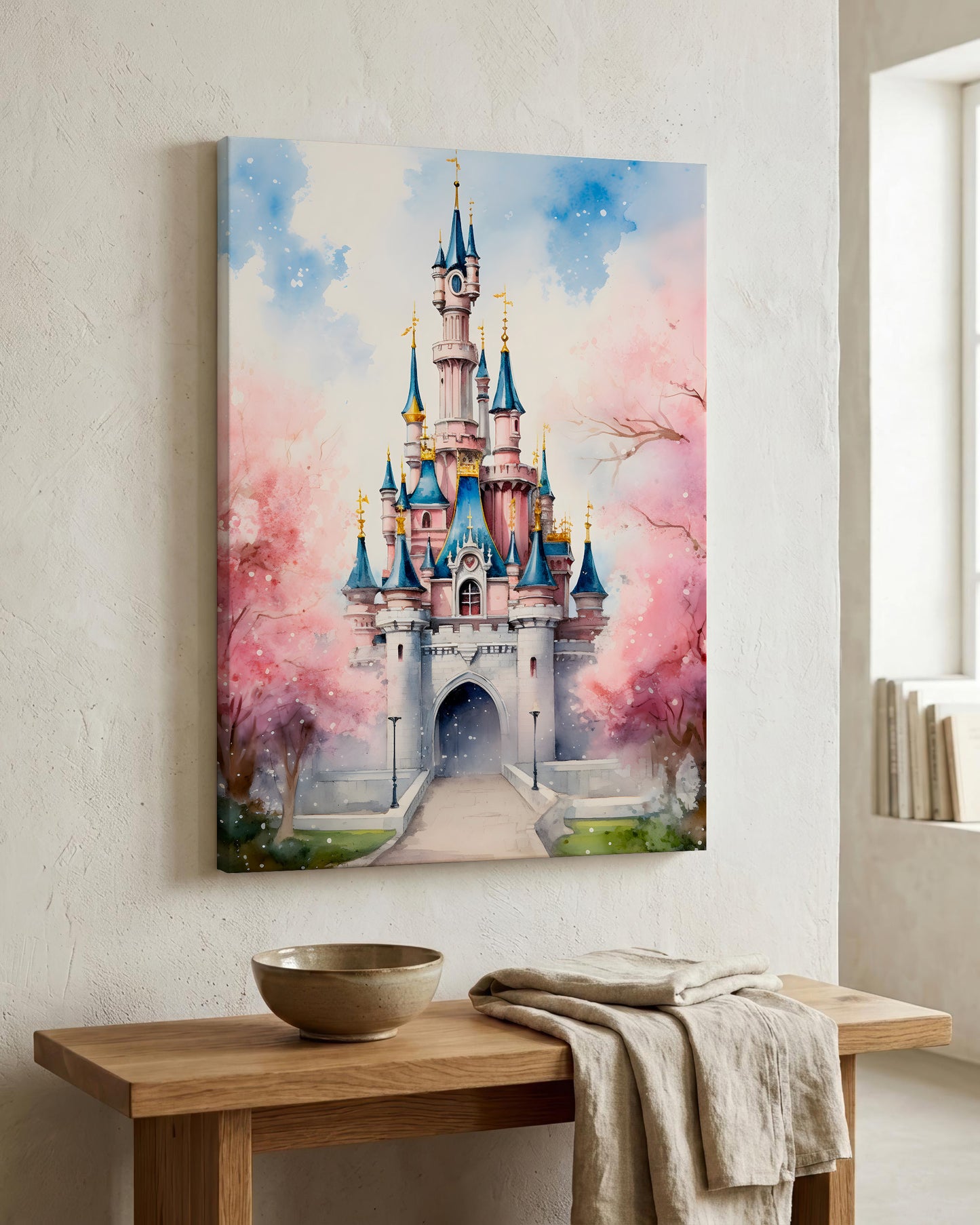 A vertical canvas wall art print depicting a whimsical fairytale castle with pink cherry blossoms, displayed on a textured white wall above a wooden console table with a bowl and linen cloth.
