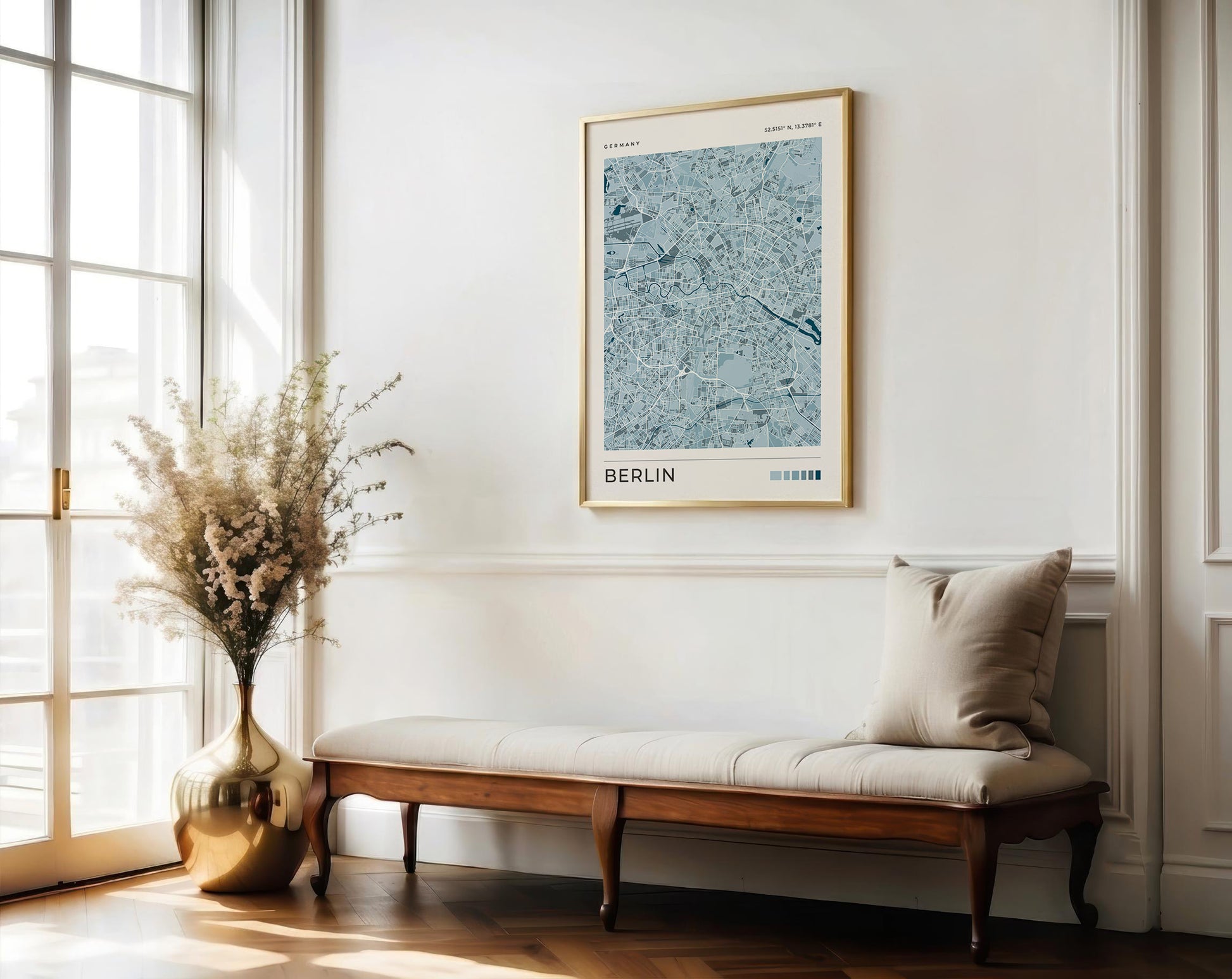 A framed art print of a light blue and gray Berlin street map hangs on a white wall above a wooden bench with a beige cushion in a bright, modern room.