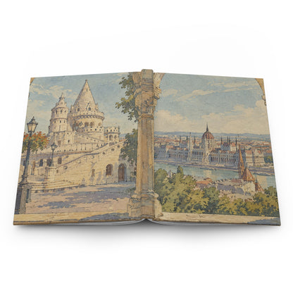 An open vintage book or art print displaying a scenic watercolor illustration of Budapest, featuring the Fisherman's Bastion and the Hungarian Parliament House across the Danube River, set against a plain white background.