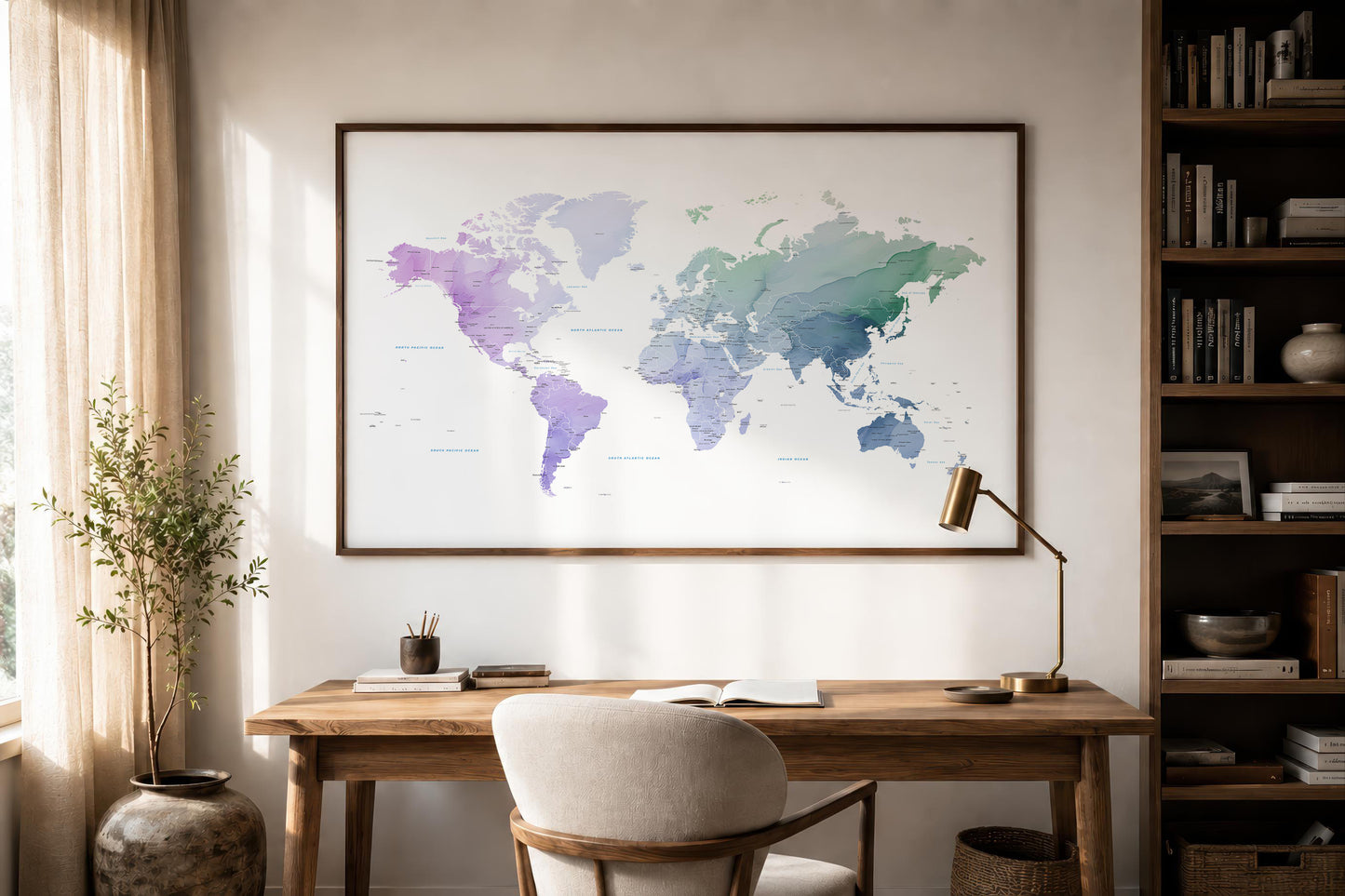 A framed world map print with watercolor-style continents in purple, blue, and green tones, displayed on a wall above a wooden desk in a styled home office setting.