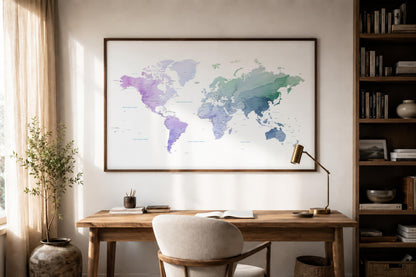 A framed world map print with watercolor-style continents in purple, blue, and green tones, displayed on a wall above a wooden desk in a styled home office setting.