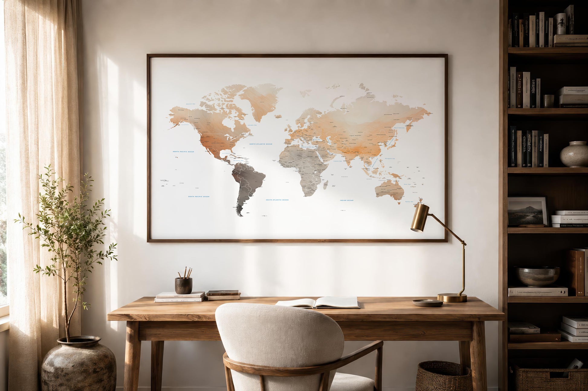 A large framed world map print with a watercolor-style design hangs on a wall above a wooden desk in a styled home office setting with a chair, lamp, and bookshelves.