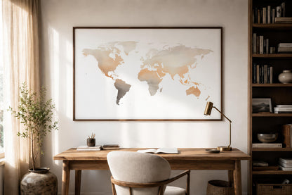 A large framed world map print hangs on a light beige wall above a wooden desk in a styled home office. The map features continents in soft warm beige, tan, and gray tones on a white background, enclosed in a thin dark frame.