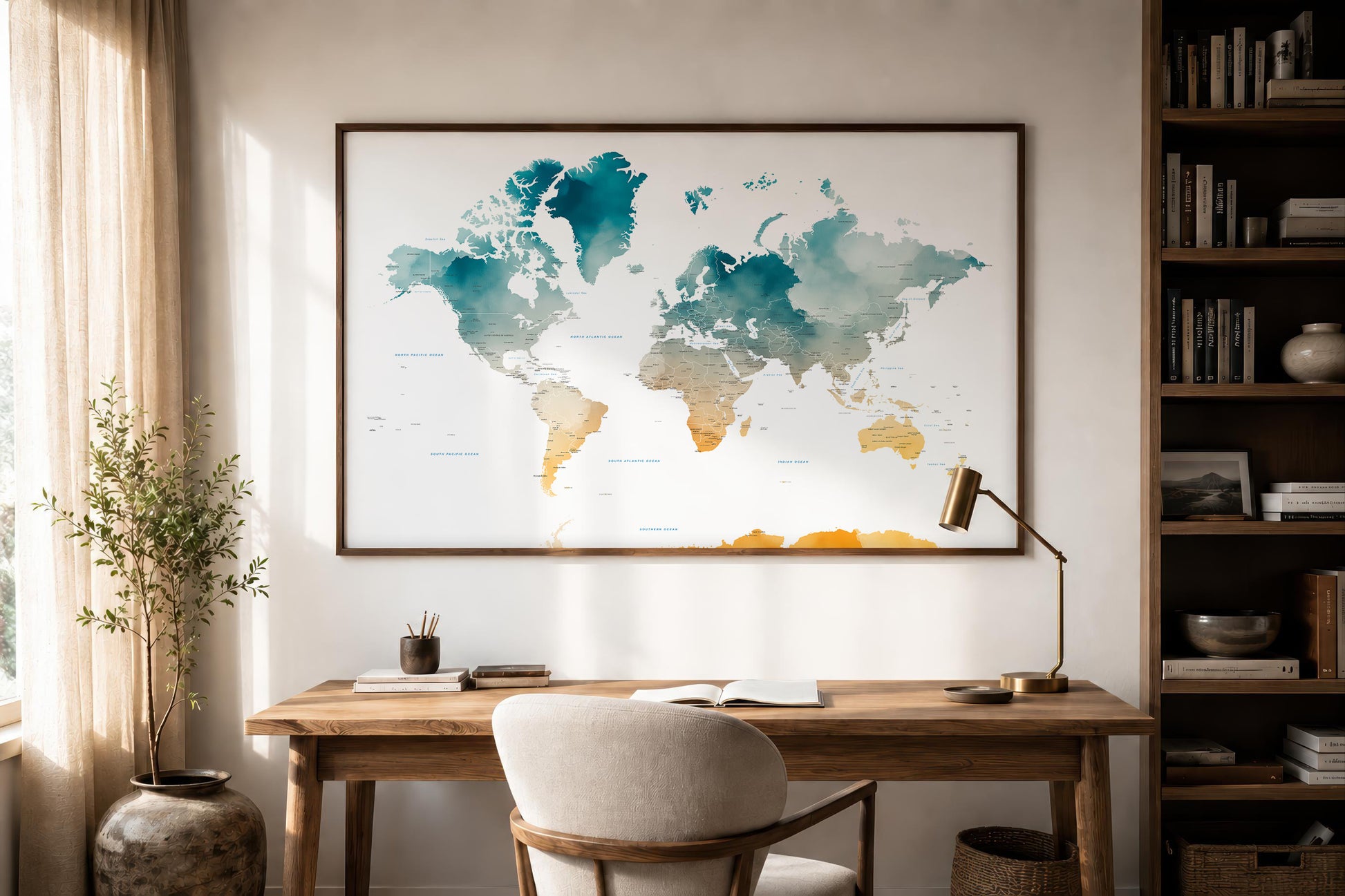 A framed world map print with teal, blue, and gold watercolor-style continents hanging on a wall above a wooden desk in a styled home office.