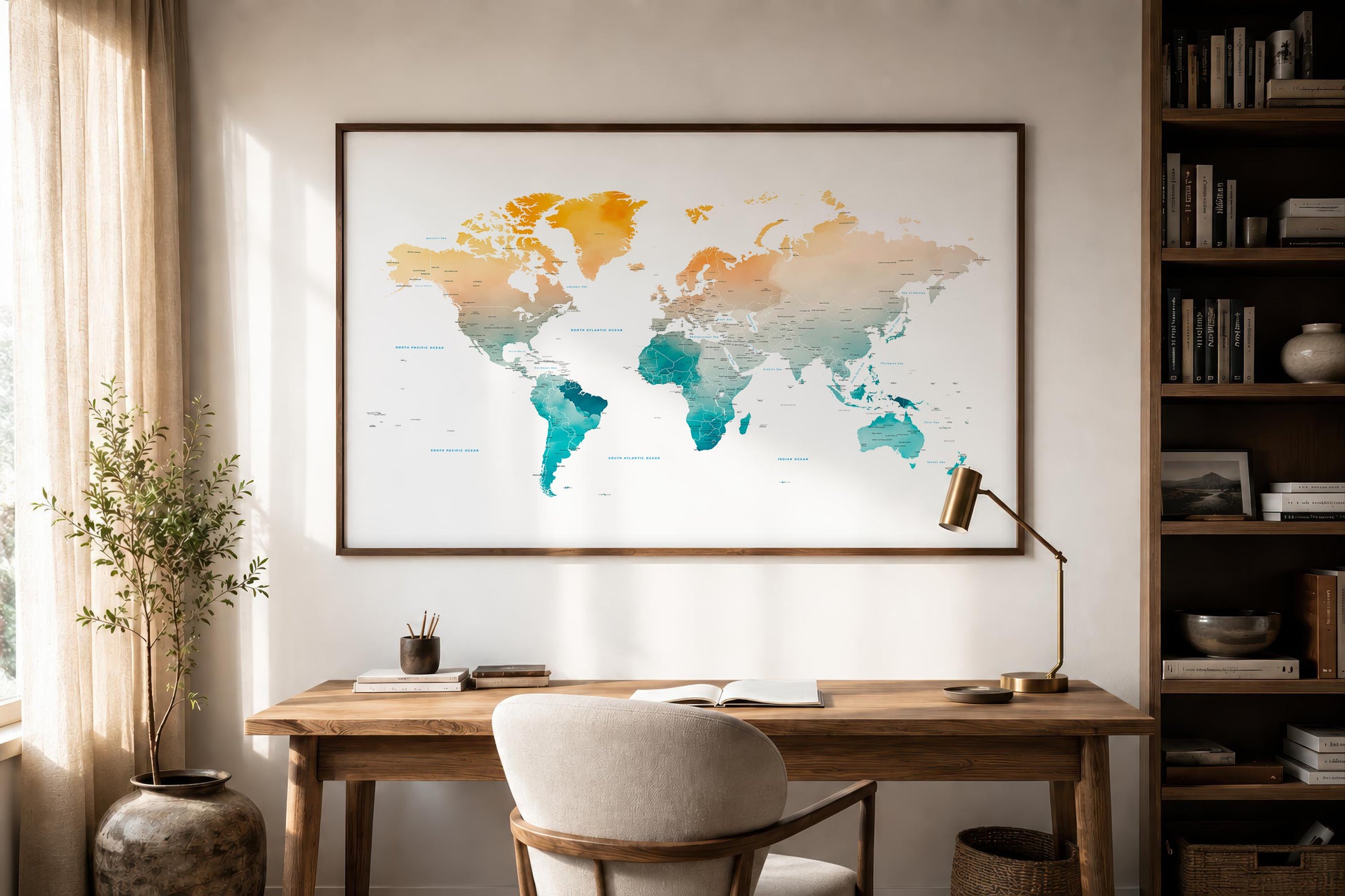 A framed world map art print with a watercolor gradient in orange, yellow, and teal, hanging on a beige wall above a wooden desk in a modern, sunlit home office.