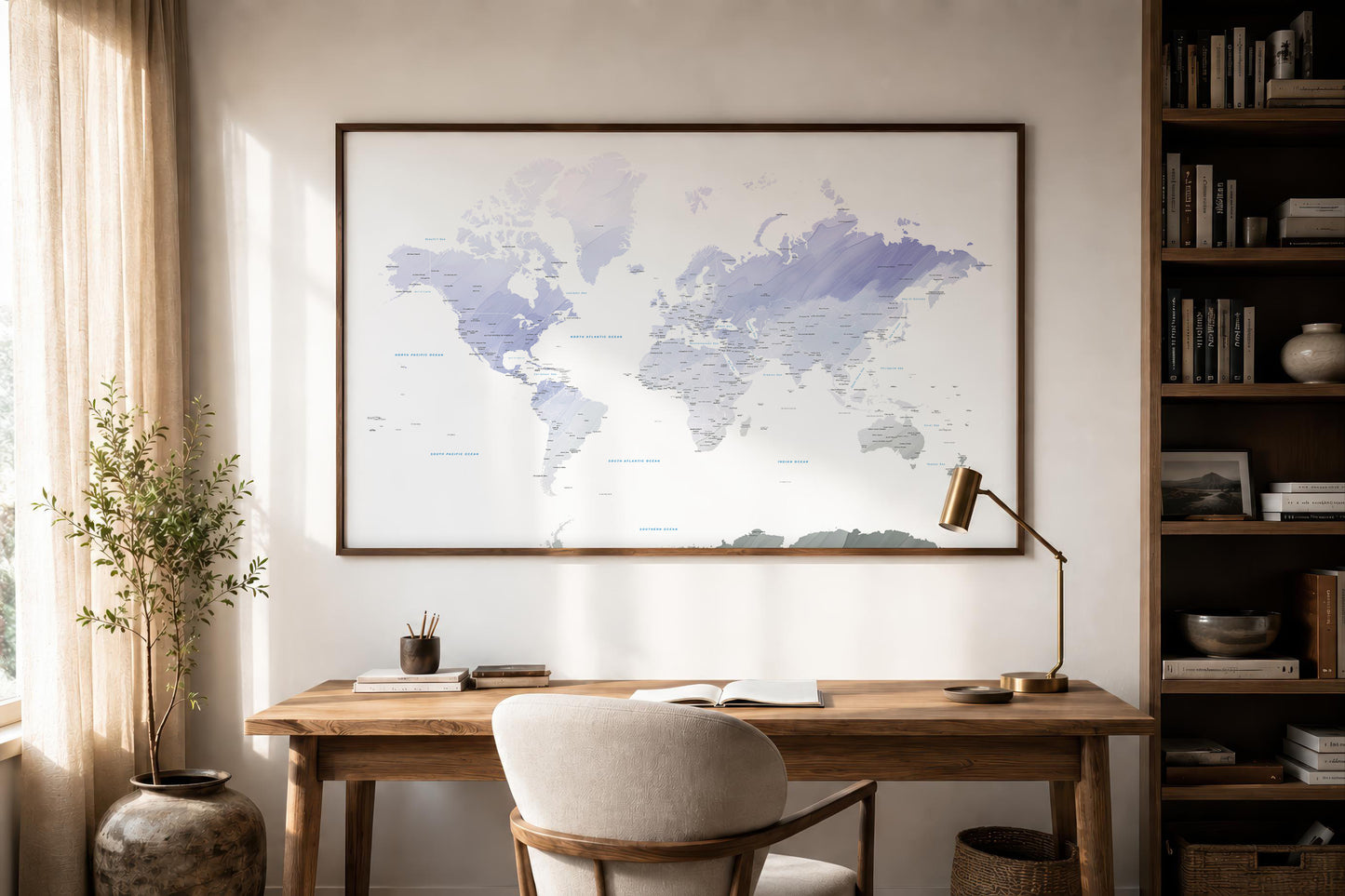 A large framed world map print with soft blue and purple watercolor-style landmasses hangs on a light beige wall above a wooden desk in a styled home office setting.
