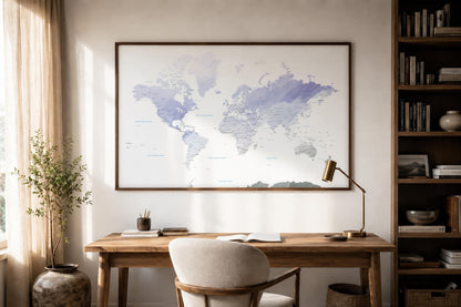 A large framed world map print with soft blue and purple watercolor-style landmasses hangs on a light beige wall above a wooden desk in a styled home office setting.