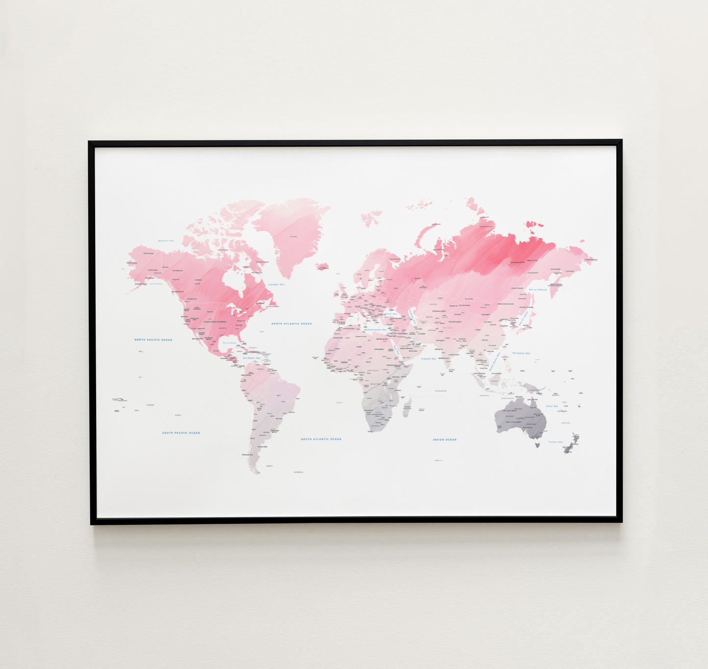 Pink watercolor world map wall art in a black metal frame.