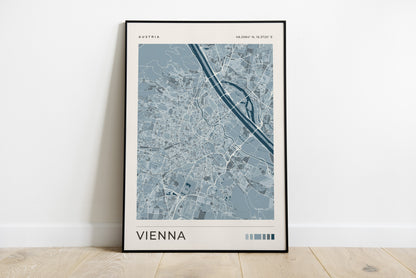 A framed minimalist city map print of Vienna, Austria, leaning against a white wall on a light wood floor.
