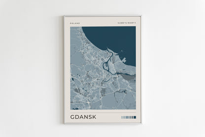 A framed minimalist map poster of Gdansk, Poland, featuring a light blue and gray street layout with a dark teal sea area, mounted on a clean white wall.