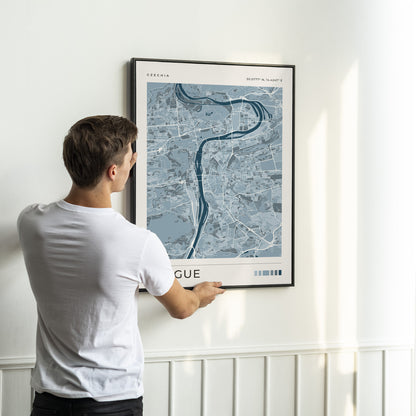 A man in a white t-shirt is shown from behind, adjusting a framed map print of Venice, Italy, on a white wall with wainscoting.