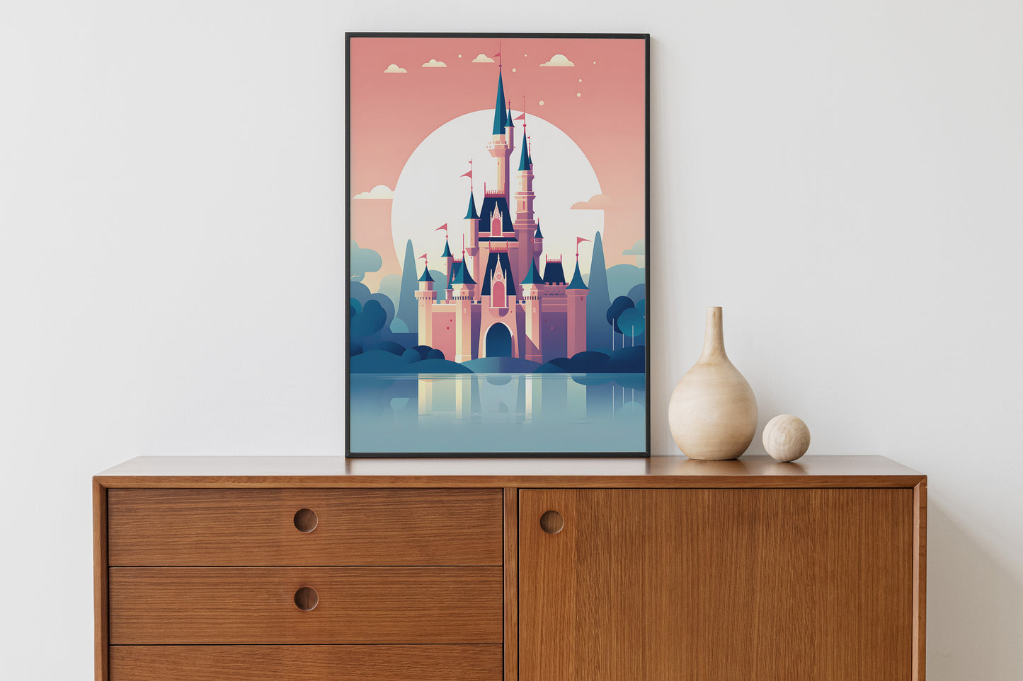 A framed art print of a stylized fairytale castle in a pink and blue landscape, displayed on a wooden sideboard next to two decorative vases against a white wall.