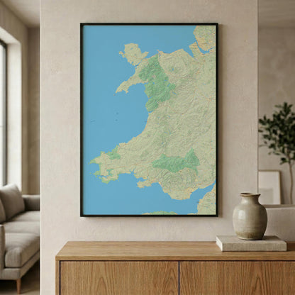 A framed topographic map print of Wales hangs on a beige wall above a wooden console table in a modern living room setting.