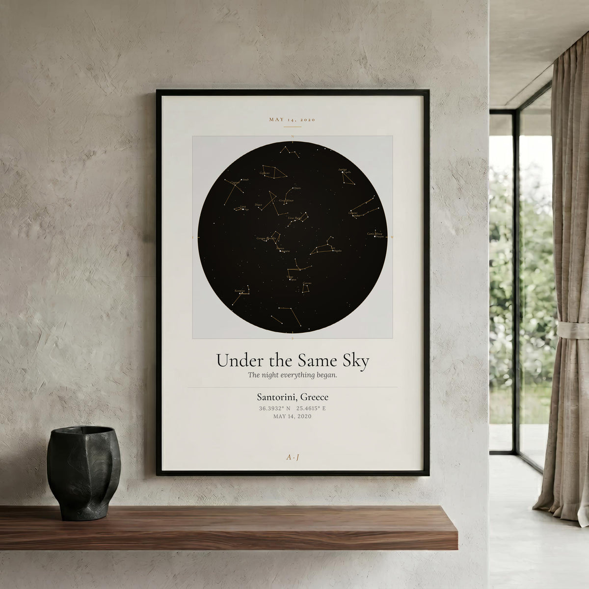 A framed minimalist celestial poster hanging on a textured light gray wall above a wooden shelf. The poster features a large black circle with constellation lines and the title 'Under the Same Sky' with location and date details below.