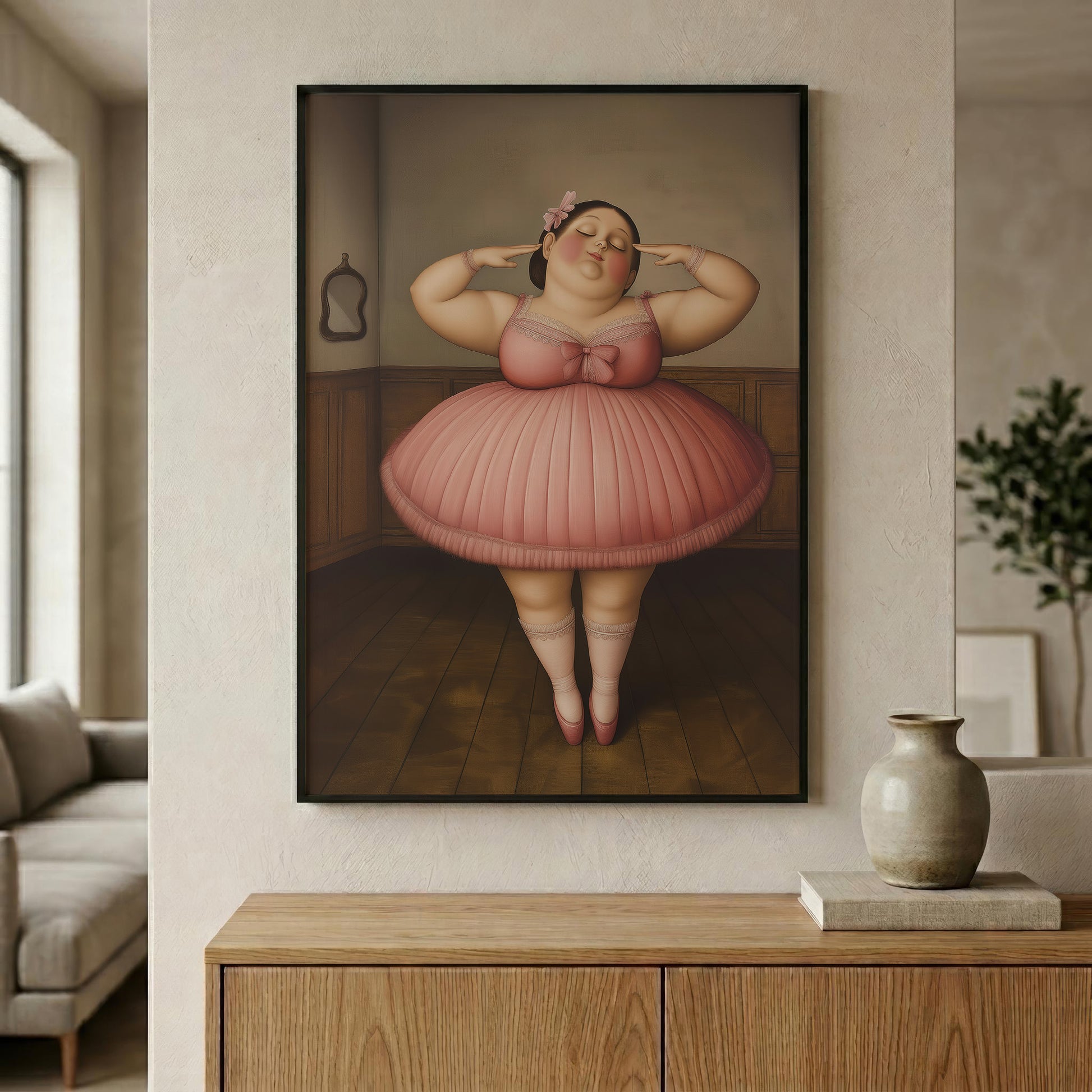 A framed wall art print hanging on a beige wall above a wooden console table. The artwork depicts a stylized figure in a pink tutu standing in an interior with warm brown wood paneling and floor.