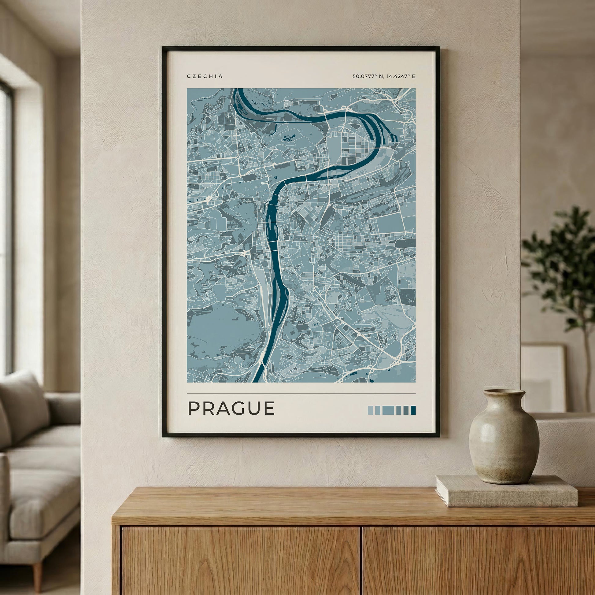 A framed art print of a light blue and gray map of Prague, featuring the Vltava River, displayed on a beige wall above a wooden console table in a modern living room setting.