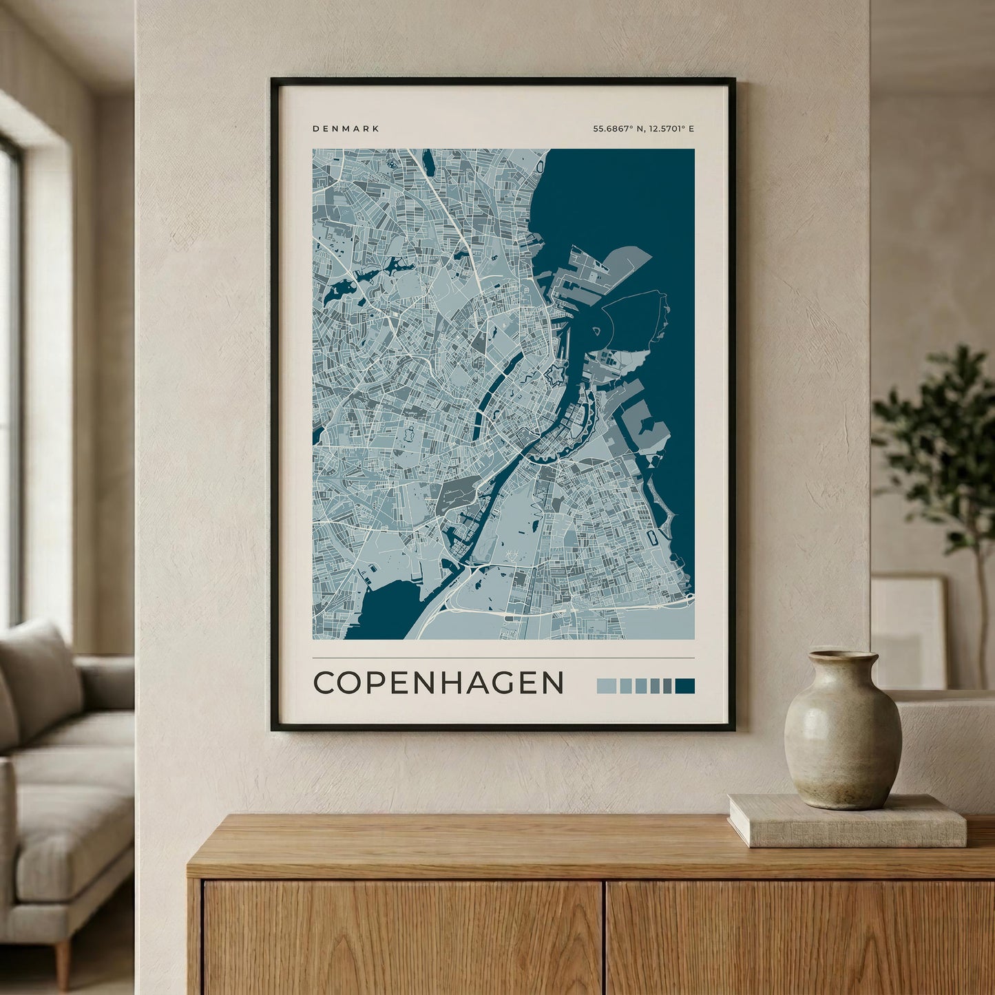 A framed Copenhagen city map print hangs on a beige wall above a wooden console table in a modern living room setting.