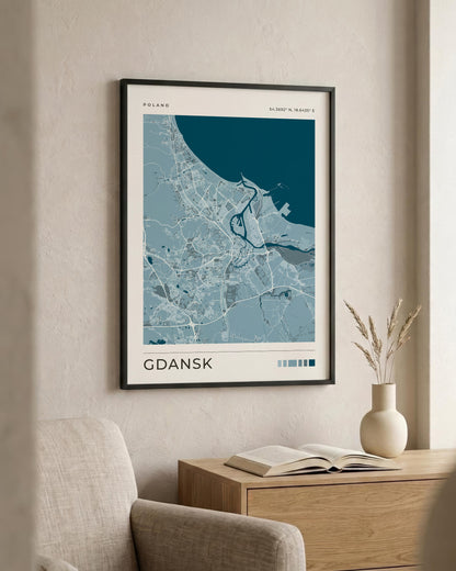 A framed minimalist map print of Gdansk, Poland, featuring shades of blue and white on a cream background, styled in a warm, modern living room setting above a wooden console table.