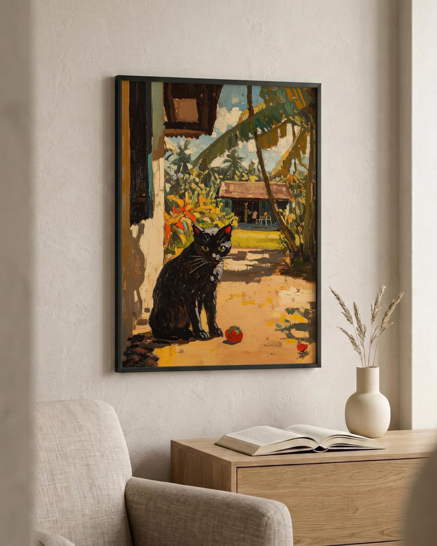 A framed art print depicting a black cat in a tropical garden setting, hanging on a beige wall above a wooden console table with an open book and a vase.