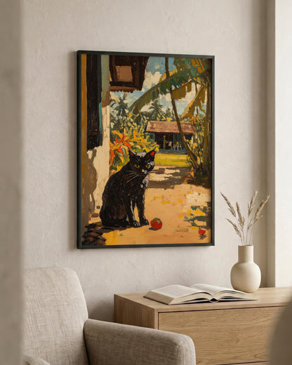 A framed art print depicting a black cat in a tropical garden setting, hanging on a beige wall above a wooden console table with an open book and a vase.