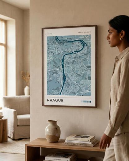 A framed blue map poster of Bucharest, Romania, hanging on a beige wall in a modern, sunlit living room. A woman in a beige linen outfit is standing to the right, looking at the print.